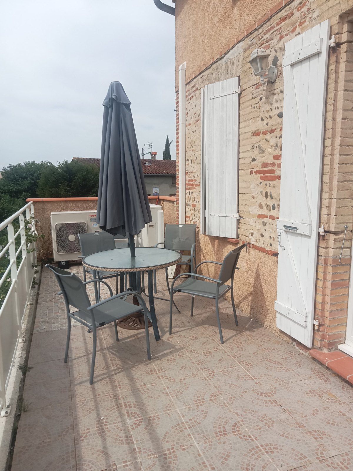 La terrasse avec sa table, ses chaises et son parasol, devant la façade en brique